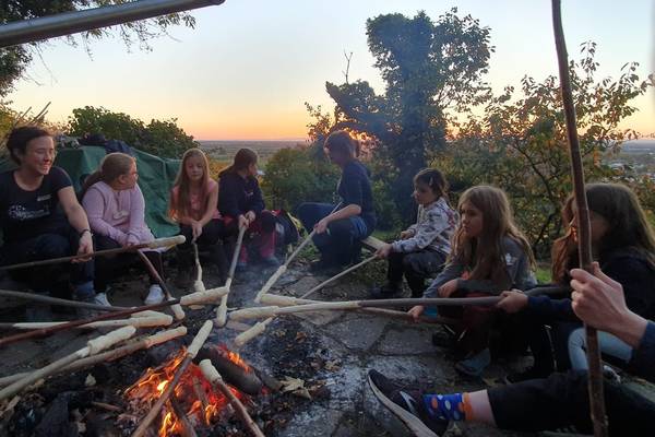 Kinder die um ein Lagerfeuer sitzen und Stockbrot machen